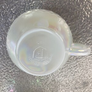 May include: White iridescent ceramic mug with a handle. The bottom of the mug has the text "HEIRLOOM PROOF" and a logo with the letter "E" inside a shield. The text "USA" is also visible.