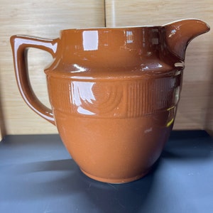 May include: A brown ceramic jug with a textured design. The jug has a wide mouth and a handle.