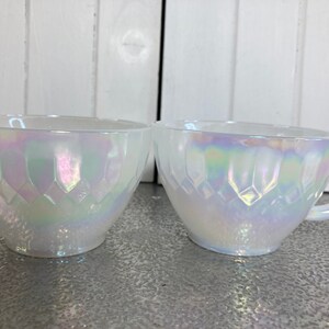 May include: Two white iridescent glass cups with a diamond pattern. The cups are on a white surface.