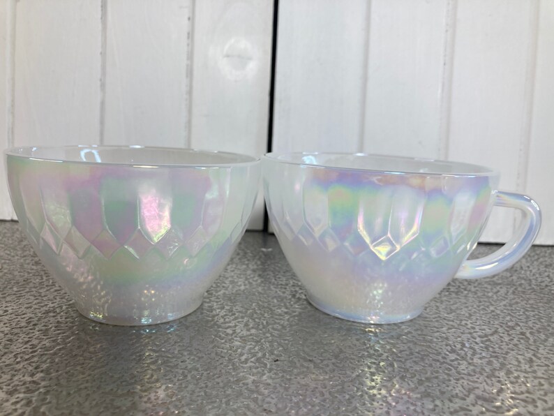 May include: Two white iridescent glass cups with a diamond pattern. The cups are on a white surface.