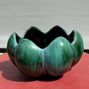 May include: A green ceramic planter with a wavy, scalloped rim and a rounded, bulbous shape. The planter has a dark green glaze with a light green swirl pattern.