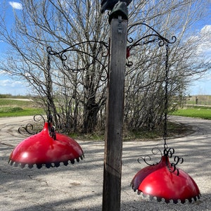 May include: Two red hanging light fixtures with black trim and a decorative metal design hang from a wooden post with a black metal owl perched on top.