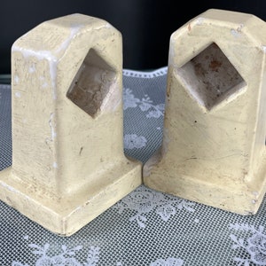 Può includere: Un paio di ferma libri in ceramica vintage di colore giallo pallido. Ogni ferma libri presenta un'apertura a forma di diamante al centro.