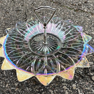 May include: A clear glass serving tray with a silver handle. The tray has a scalloped edge and an iridescent finish.