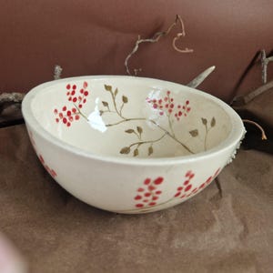 Puede incluir: Un tazón de cerámica blanca con un diseño pintado a mano de bayas rojas y ramas marrones.