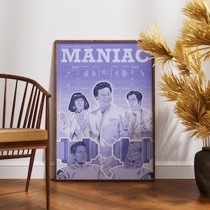 May include: A framed poster featuring the word "MANIAC" in large, white, pixelated letters. The poster has a purple background and depicts several people. The poster is leaning against a wall next to a wooden chair and decorative vase.