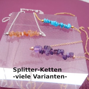 May include: Three necklaces with different coloured gemstones. The necklaces are on a clear display stand. The text "Splitter-Ketten -viele Varianten- " is on the display stand.