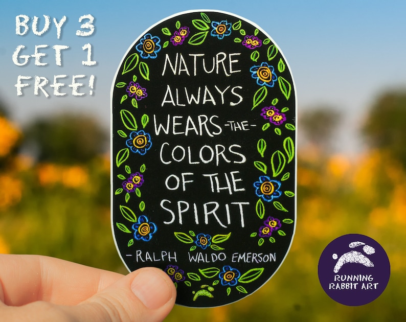 May include: Black and white sticker with a quote by Ralph Waldo Emerson: "Nature always wears the colors of the spirit." The sticker is surrounded by colorful flowers and leaves. The sticker is held in a hand against a blurred background of yellow and green.