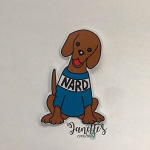 May include: A brown cartoon dog wearing a blue sweater with the word "NARD" in white letters. The dog is sitting with its tongue sticking out. The image has a white background and the text "Janettes creations" in cursive.