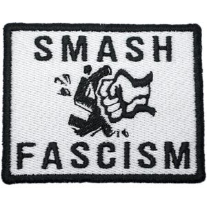 Puede incluir: Un parche rectangular con las palabras "SMASH FASCISM" en letras mayúsculas negras en negrita. Un gráfico en blanco y negro de un puño rompiendo un símbolo está en el centro. El parche tiene un fondo blanco y un borde negro.
