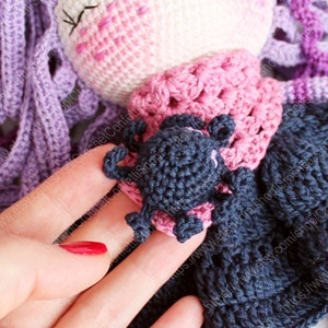 K&ouml;nnte beinhalten: Eine geh&auml;kelte Puppe mit lila Haaren, einem rosa Kleid und einer schwarzen geh&auml;kelten Spinne auf der Schulter.