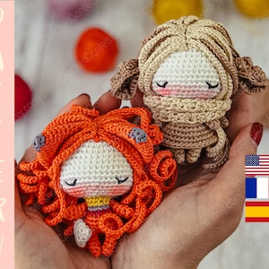 Puede incluir: Dos muñecas de crochet con los ojos cerrados. La muñeca de la izquierda tiene el pelo naranja y un vestido rojo. La muñeca de la derecha tiene el pelo marrón y un vestido marrón. Las muñecas están siendo sostenidas en las manos de una persona.
