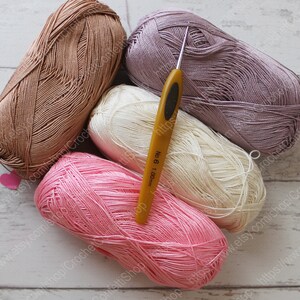 May include: Four balls of yarn in pink, beige, white, and purple colors, with a yellow crochet hook labeled "No. 6 1.00mm".