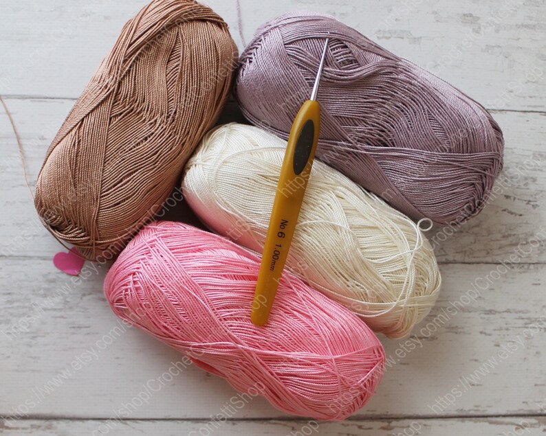 May include: Four balls of yarn in pink, beige, white, and purple colors, with a yellow crochet hook labeled "No. 6 1.00mm".
