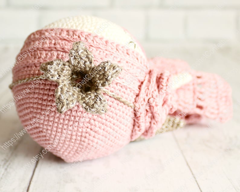 Op de afbeelding: Een roze en cr&egrave;me gebreide baby muts met een bruin gebreid bloemenaccent. De muts is gemaakt van zacht garen en is perfect voor een pasgeboren baby.