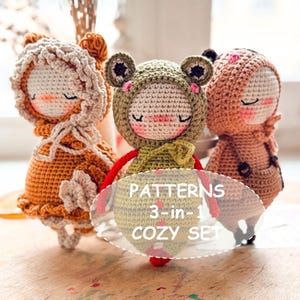 May include: Three crocheted amigurumi dolls, a brown doll with a white crocheted hood, a green frog doll with a brown crocheted hood, and a pink doll with a brown crocheted hood. The dolls are sitting on a wooden surface. The text "PATTERNS 3-in-1 COZY SET" is visible in the image.