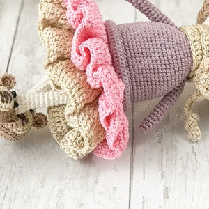 May include: A crocheted doll wearing a pink and beige dress with a purple top and a brown crocheted monkey attached to its arm.