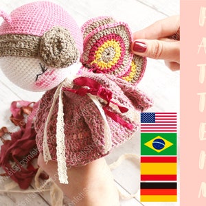 May include: Crocheted amigurumi doll with a pink and brown head, a pink and yellow butterfly wing, and a pink dress with white lace trim. The doll is holding a red ribbon. The image also includes the text "PATTERN" and flags of the United States, Brazil, and Germany.