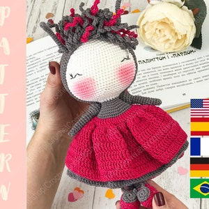 May include: Crocheted doll with gray hair, a pink dress, and a gray and white body. The doll is holding a book with the text "Paddington and Pardon". The image also includes flags of the United States, Spain, France, Germany, and Brazil.