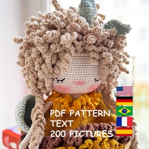 Op de afbeelding: Een handgemaakte gehaakte pop met krullend beige haar, gesloten ogen en een roze blos. De pop draagt een gele en bruine jurk. De tekst "PDF PATTERN TEXT 200 PICTURES" is zichtbaar.