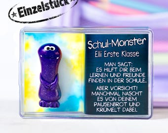 May include: A purple glittery monster figurine in a clear case. The figurine has a smiling face and arms crossed over its chest. Text on the case reads "Schul-Monster" and "Einzelstück". The background is a mix of yellow and blue.