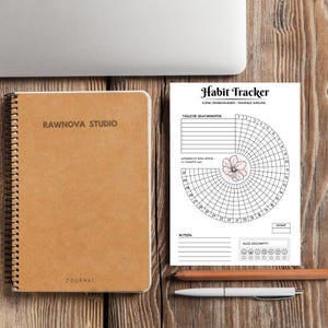 May include: A spiral-bound journal and a habit tracker sheet on a wooden surface. The journal is tan with the text "RAWNOVA STUDIO" and "JOURNAL". The habit tracker has a floral design and the words "Habit Tracker". A pen and pencil are also present.
