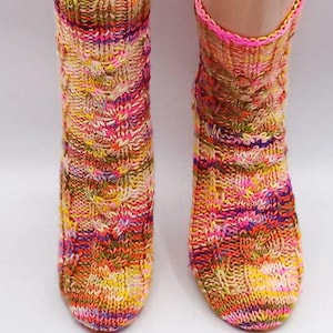 Könnte beinhalten: Ein Paar bunte handgestrickte Socken mit einem mehrfarbigen Muster. Die Socken sind aus verschiedenen Farbtönen von Rosa, Orange, Gelb, Grün und Lila gefertigt.