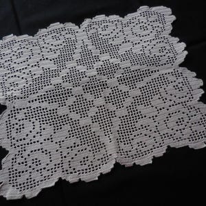 Könnte beinhalten: Weißes gehäkeltes Deckchen mit detailliertem Blumenmuster. Das quadratische Deckchen hat einen gewellten Rand und wird vor einem schwarzen Hintergrund präsentiert. Das komplizierte Design ist im gesamten Stück sichtbar und zeigt die filigrane Handwerkskunst.