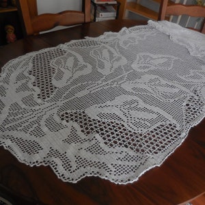 Könnte beinhalten: Weißer gehäkelter Tischläufer mit Blumenmuster. Der Läufer ist aus zarter Spitze gefertigt und zeigt ein sich wiederholendes Muster aus Blumen.