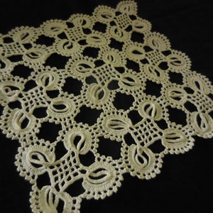 Könnte beinhalten: Eine zarte, cremefarbene Häkeldeckchen mit einem sich wiederholenden Muster aus filigranen Blumendesigns. Die Deckchen ist aus feinem Garn gefertigt und hat eine zarte, spitzenstichelige Optik.