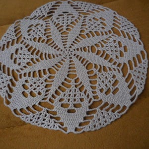 Può includere: Un delicato centrino all'uncinetto di colore lilla chiaro con un design circolare. Il centrino ha un centro con un motivo a stella e un pizzo intricato attorno ai bordi.