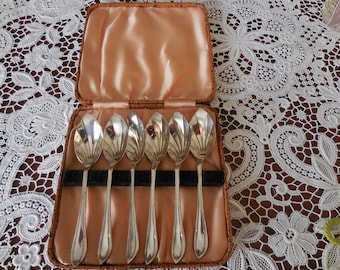 May include: Set of six silver teaspoons in a brown velvet-lined case. The spoons have a decorative, fan-shaped design.