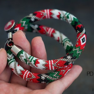 May include: Two beaded bracelets with a red, white, green, and black geometric pattern. The bracelets are made with small seed beads and have silver metal clasps.  PDF pattern MRF jewelry.
