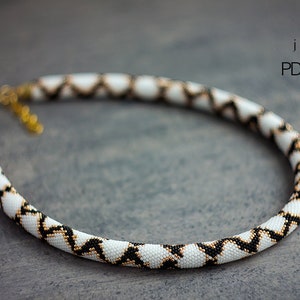 May include: A white, black, and gold beaded necklace with a geometric pattern. The necklace is on a gray background. MRF jewelry PDF pattern.