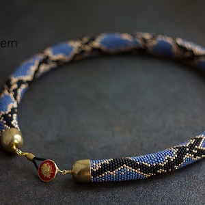 May include: A blue, black and gold beaded necklace with a snake skin pattern. The necklace is made with small beads and has a clasp closure.