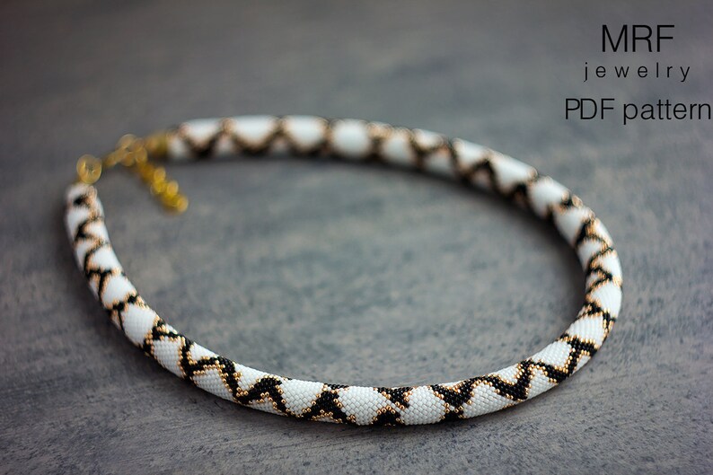 May include: A white, black and gold beaded necklace with a geometric pattern. The necklace is on a grey background. MRF jewellery PDF pattern.