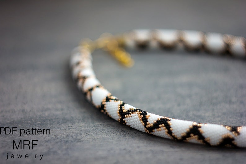 May include: A white, black and gold beaded necklace with a geometric pattern. The necklace is made with small seed beads and is approximately 18 inches long.