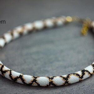 May include: A white, black and gold beaded necklace with a geometric pattern. The necklace is made with small seed beads and is approximately 18 inches long.