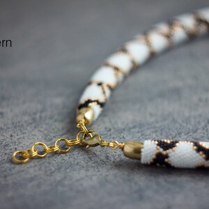 May include: A white and black beaded necklace with a gold clasp. The necklace is made with small beads in a geometric pattern.