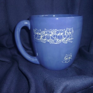 Könnte beinhalten: Eine blaue Keramiktasse mit einem weißen Eulen-Design. Die Eulen sind in einer Reihe angeordnet und haben ein verspieltes Aussehen.
