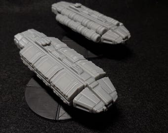 May include: Two gray, detailed, miniature spaceships on black bases. The spaceships have a long, rectangular shape with a pointed front and a series of small, rectangular windows along the sides.