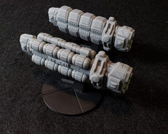 May include: Two gray 3D printed spaceship models on a black base. The models are detailed with various compartments and panels.