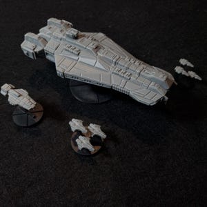 Op de afbeelding: Een grijs ruimtevaartuigmodel met een lange, puntige neus en een gedetailleerd ontwerp. Het ruimtevaartuig staat op een zwarte basis en is omringd door kleinere grijze ruimtevaartuigmodellen op zwarte bases.