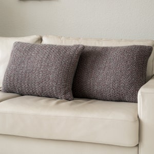 Könnte beinhalten: Zwei graue Kissen mit einem dezenten geometrischen Muster auf einem weißen Ledersofa.