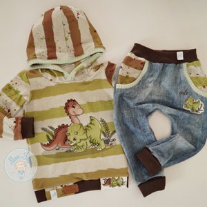 Peut inclure: Un sweat à capuche rayé vert et marron avec un motif de dinosaure et un pantalon en jean bleu et marron assorti avec un patch de dinosaure. Le pantalon a une ceinture marron et des poignets marrons.