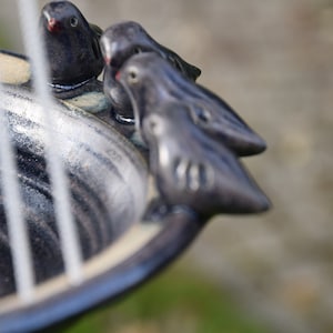 May include: A black ceramic bird bath with three small black ceramic birds perched on the rim.