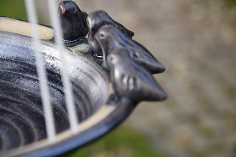 May include: A black ceramic bird bath with three small black ceramic birds perched on the rim.