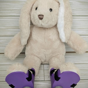 May include: A beige plush bunny with long white ears wearing purple and black roller skate shoes.