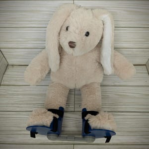 May include: A beige plush bunny with long white ears wearing blue and white roller skate shoes.