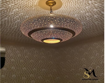 May include: A gold-toned, round, Moroccan pendant light fixture with a decorative, intricate, perforated pattern. The light fixture has three tiers and casts a patterned shadow on the ceiling.